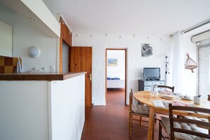 A kitchen with a wooden counter, a dining area with a table and chairs, a television, and a bed in the background. - El Tiburon N°17 - À 250 m de la plage (Argeles-sur-Mer)