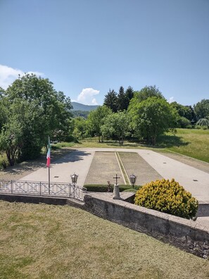 A landscaped area with a flag, lamp posts, and a cross monument. - Former San Giorgio Parish House between beautiful Lake Como and Lake Lugano (Pellio Intelvi)