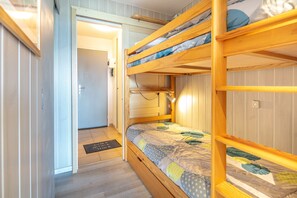 Habitación con literas, una puerta que da a otra habitación, una mesita de noche y un tapete en el suelo.