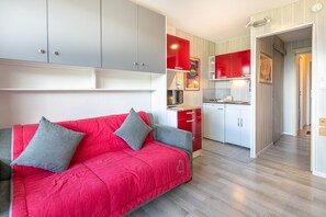 Una cocina moderna con armarios rojos, un sofá gris con cojines grises y piso de madera.