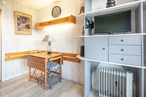 Una habitación con un escritorio de madera, una lámpara, un televisor en un estante y un radiador.