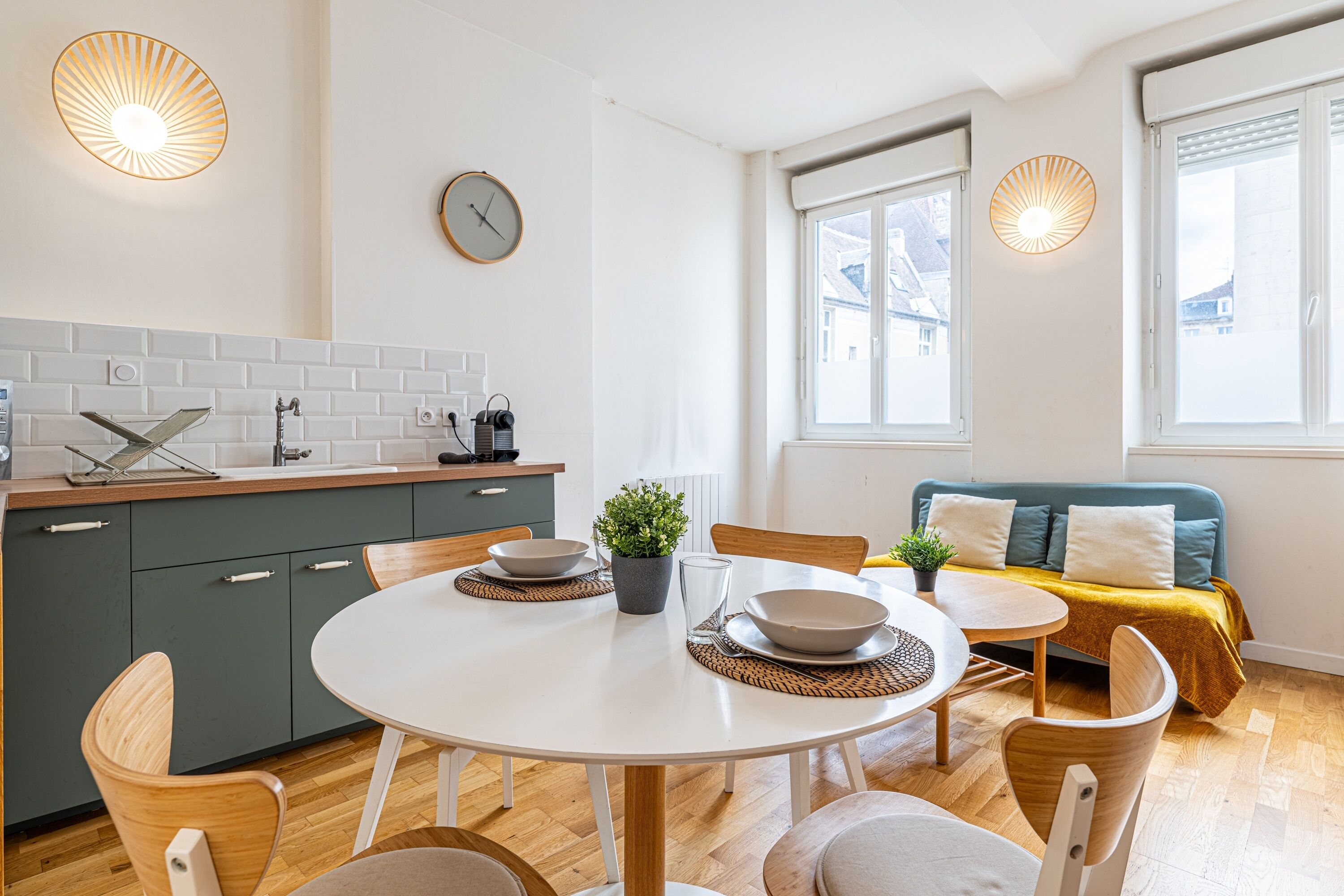 Cocina moderna con salpicadero de ladrillo blanco, armarios de madera y comedor con mesa y sillas redondas.