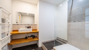 Ein modernes Badezimmer mit einem weißen Waschbecken, Holzböden, einer Duschkabine aus Glas und einer gefliesten Duschwand.