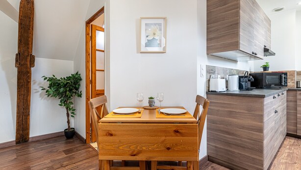 Een eetgedeelte met een houten tafel en stoelen, een potplant en een keuken met houten keukenkastjes en apparatuur.