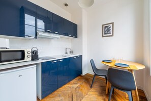 A compact kitchen with dark blue cabinets, a white countertop, a microwave, a small refrigerator, and a dining area with two chairs and a table. - Nadal - Dans l'hypercentre de Caen (Caen)