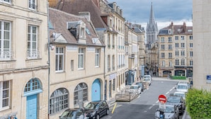 A street view with historic buildings, parked cars, and a church spire in the background.