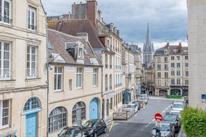 A street view with historic buildings, parked cars, and a church spire in the background.