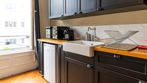 A modern kitchen with dark cabinets, a wooden countertop, a white sink, and a window with a view of buildings.