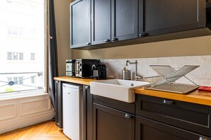 A modern kitchen with dark cabinets, a wooden countertop, a white sink, and a window with a view of buildings.