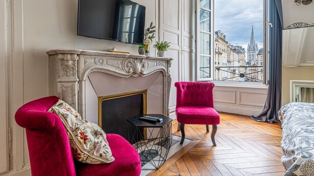 A room with a fireplace, a television, a red chair, and a large window with a view of buildings.
