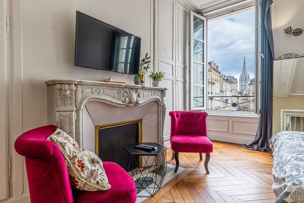 A room with a fireplace, a television, a red chair, and a large window with a view of buildings.