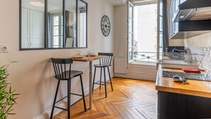 A kitchen with a wooden table, two chairs, a clock, a window, and a view of the outside.