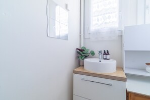 Ein Badezimmer mit einem weißen Waschbecken, einer Holz-Arbeitsplatte und einer Topfpflanze.