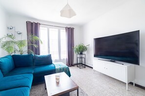 Ein Wohnzimmer mit einer Couch, einem Couchtisch, einem Fernseher und zwei Zimmerpflanzen.