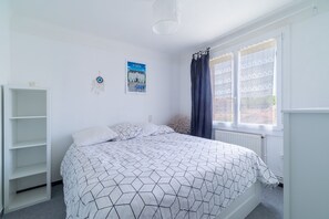 Ein Schlafzimmer mit einem Bett, einem weißen Kleiderschrank, einem Fenster mit Vorhängen, einer Heizung und einer Wand mit einem Poster.