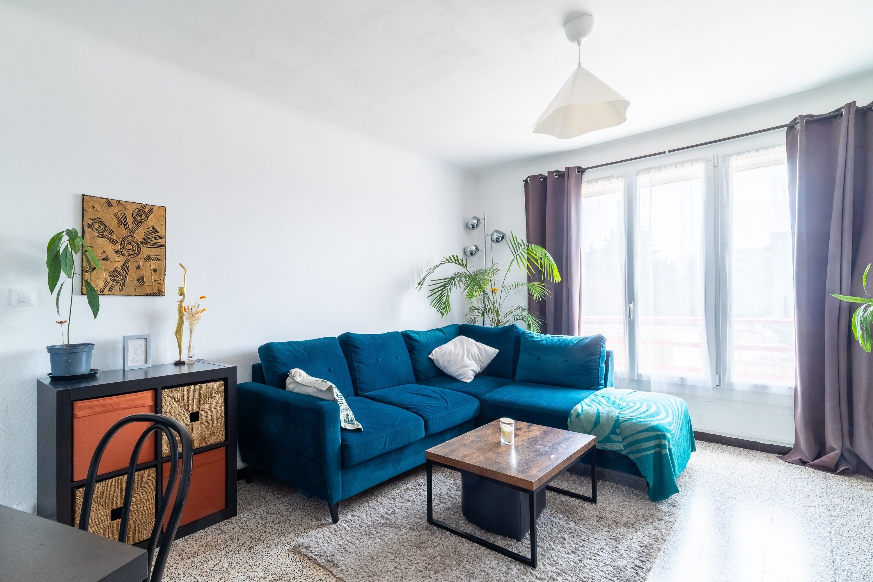 A living room with a blue sofa, a wooden coffee table, a dining table, and a decorative cabinet.