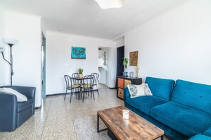 Ein Wohnzimmer mit blauem Sofa, einem Holztisch, einem Esstisch mit Stühlen und einer Lampe.