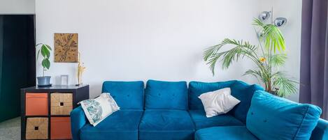 A modern living room with a blue sectional sofa, a wooden coffee table, a decorative plant, and a wall-mounted light fixture.