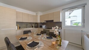 A modern kitchen with wooden cabinets, a dining table set for four, and a view of the outside through a window. - Le Bel Air du Lac - Proche centre-ville d'Annecy (Annecy)