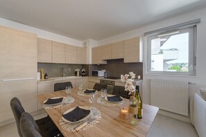 A modern kitchen with wooden cabinets, a dining table set for four, and a view of the outside through a window. - Le Bel Air du Lac - Proche centre-ville d'Annecy (Annecy)