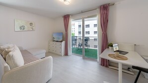 A modern living room with a sofa, a TV, a dining table with a laptop, and a view of the outside. - Le Bel Air du Lac - Proche centre-ville d'Annecy (Annecy)