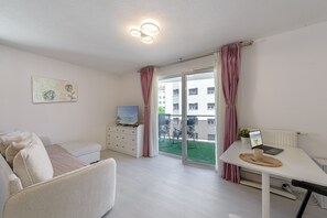 A modern living room with a sofa, a TV, a dining table with a laptop, and a view of the outside. - Le Bel Air du Lac - Proche centre-ville d'Annecy (Annecy)