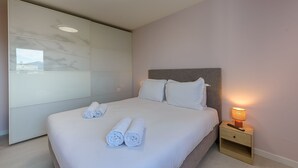 A neatly made bed with rolled white towels, a bedside lamp, and a wooden nightstand. - Le Bel Air du Lac - Proche centre-ville d'Annecy (Annecy)