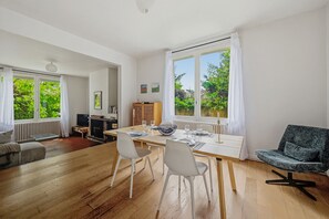 Ein moderner Wohnraum mit Essbereich, einer Couch, einem Fernseher und Blick ins Grüne.
