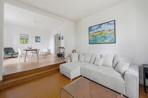 Ein modernes Wohnzimmer mit einer Eckcouch, einem Esstisch mit Stühlen und einer Treppe, die in einen anderen Raum führt.