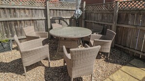 Eine Terrasse mit Korbmöbeln, einem runden Tisch und einem Holzzaun.