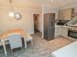 A modern kitchen with a refrigerator, microwave, stove, and dining area with chairs and a table. - 3 Railway Terrace (Bridlington)