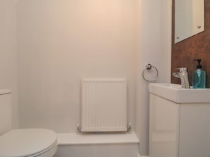 Ein Badezimmer mit Toilette, einem weißen Heizkörper, einem Waschbecken mit Spiegel und einer Seifenspender.