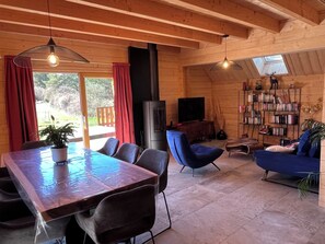Ein Holzinnenraum mit einem Esstisch, Stühlen, einer Couch, einem Fernseher und einem Bücherregal.