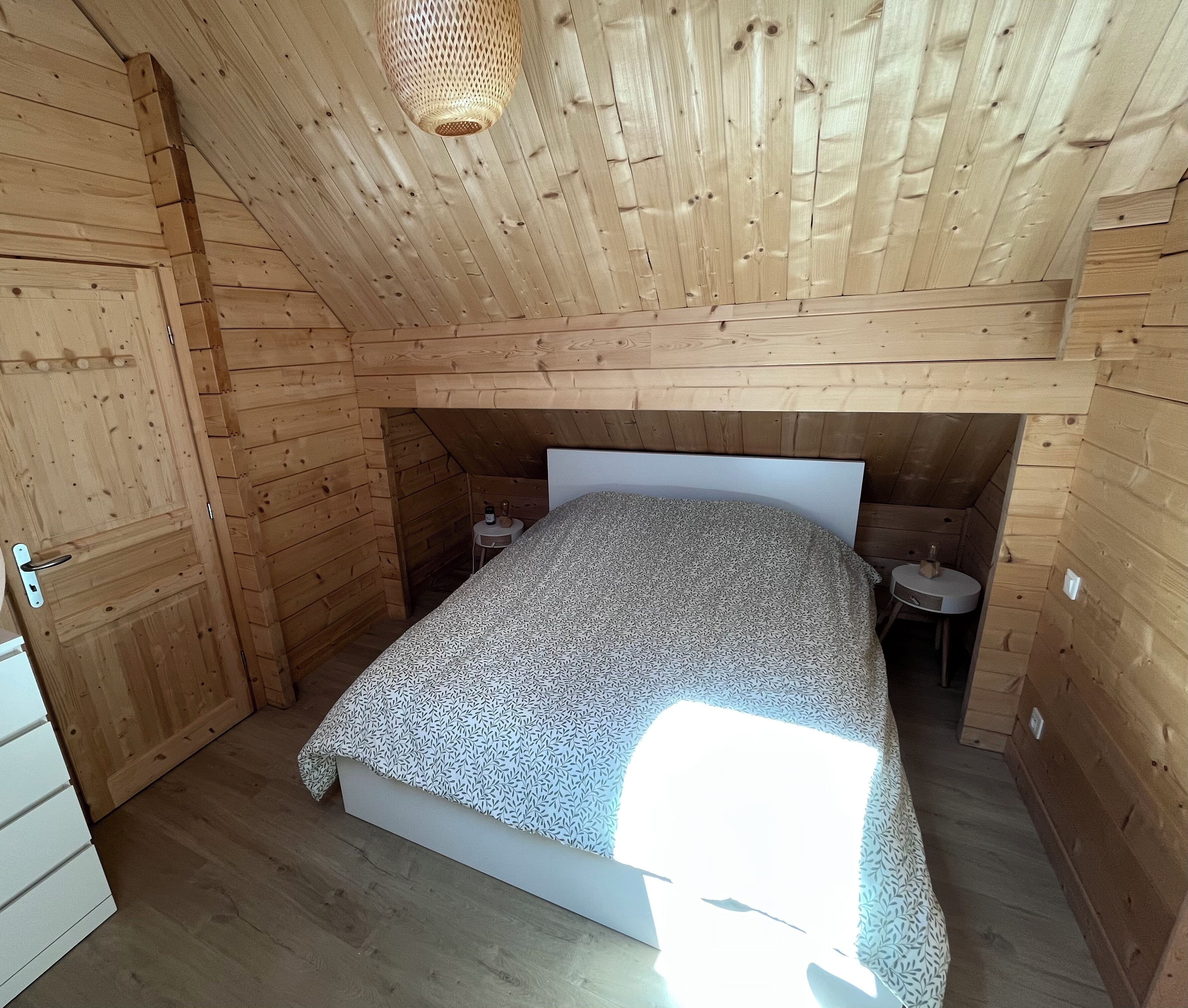 A small, wooden-paneled room with a bed, bedside tables, and a hanging light fixture.