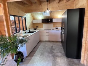Eine moderne Küche mit Holzwänden, einem schwarzen Kühlschrank, weißen Schränken, einer Spüle und einer Pendelleuchte.