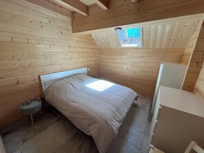 Ein kleiner, hölzerner Raum mit einem Bett, einem Tisch und einem Fenster.