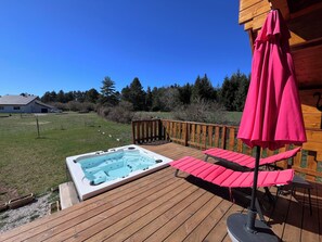 Eine Holzterrasse mit Whirlpool, Sitzgelegenheit im Freien und einem Holzzaun.