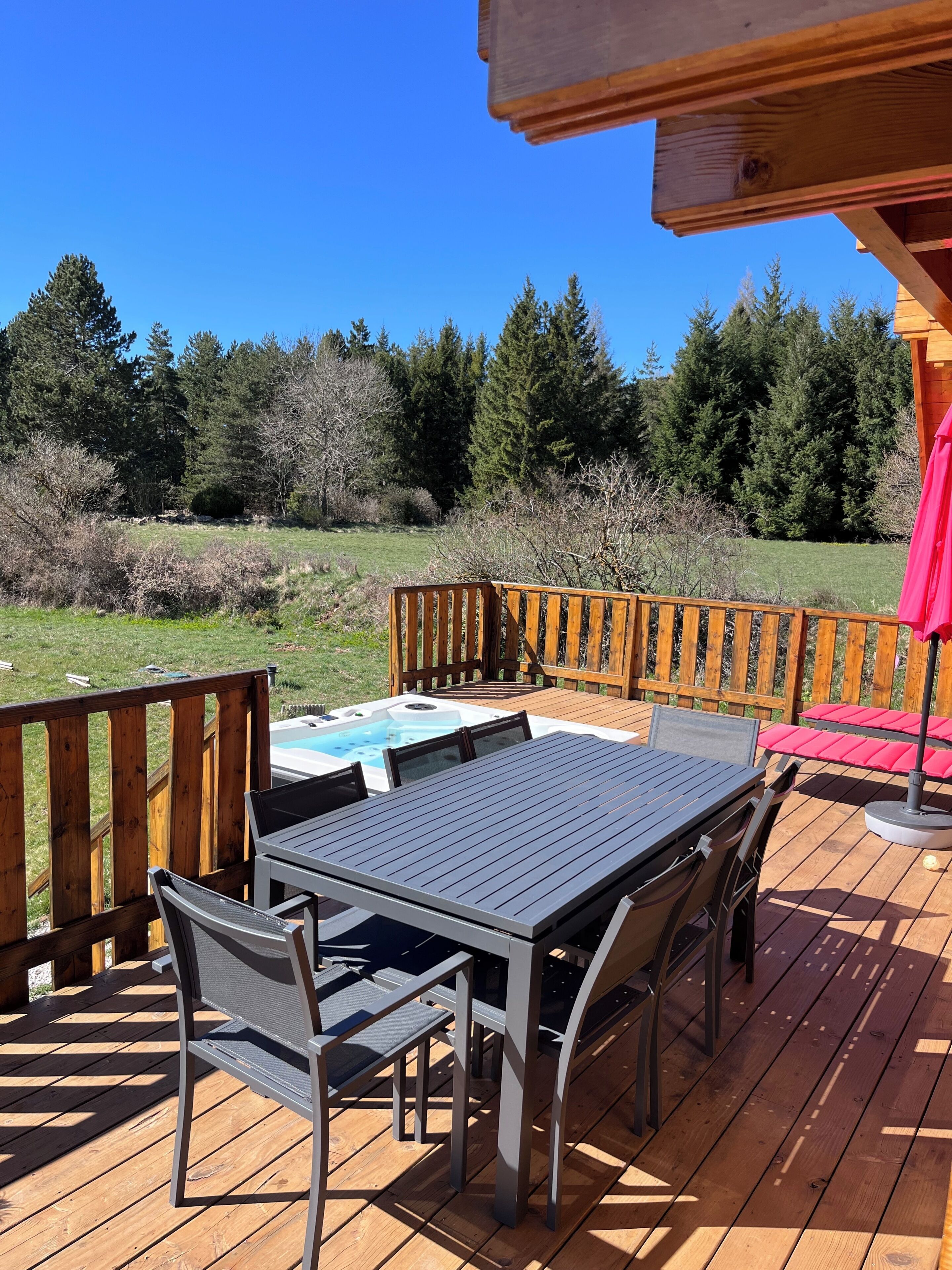 Eine Holzterrasse mit Tisch und Stühlen, einem Whirlpool und Blick auf einen Wald.