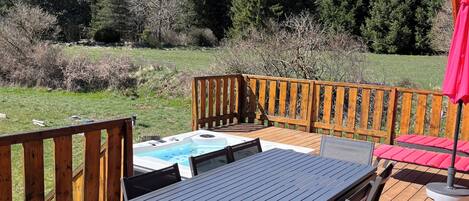 Eine Holzterrasse mit Tisch und Stühlen, einem Whirlpool und Blick auf einen Wald.