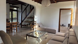 Una sala de estar con sofá, sillón y mesa de centro, una escalera y un comedor con sillas y mesa.
