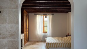 Un dormitorio con cama, ventana con cortinas, puerta de madera y pared de piedra.