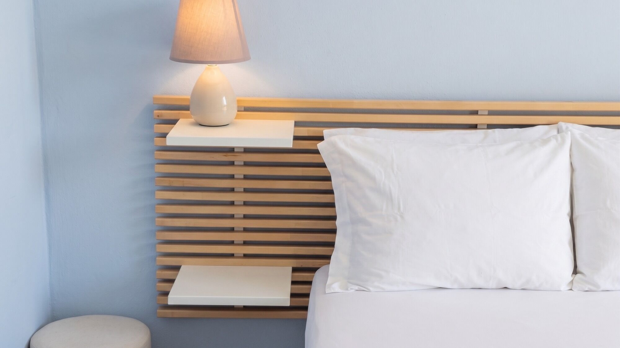 A neatly made bed with white linens, a bedside table with a lamp, and a wooden slat headboard.
