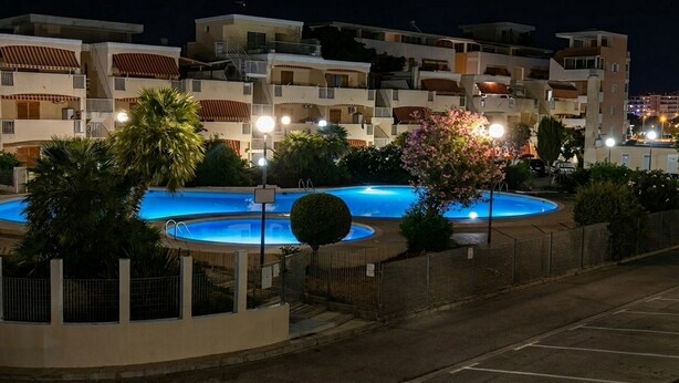 Un immeuble résidentiel doté de nombreux balcons, d’une piscine et d’un parking bien éclairé.