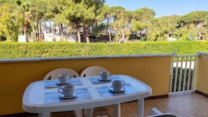 Une terrasse avec une table dressée pour quatre personnes, des sièges d’extérieur et une vue sur des arbres et une haie.