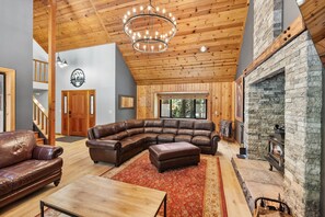 A spacious living room with a large sectional sofa, a fireplace, wooden ceiling beams, and a stone wall.