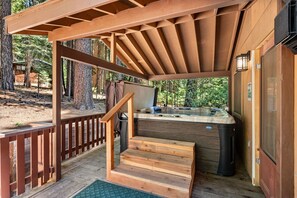 A wooden deck with a hot tub, wooden steps, and a pergola.
