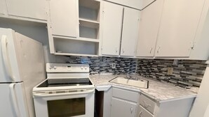 Una cocina con armarios blancos, estufa, lavaplatos y salpicadero con azulejos negros y grises.