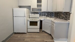Una cocina compacta con electrodomésticos blancos, salpicadero de azulejos y piso de madera.