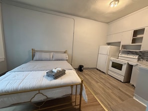 Une petite piĂšce compacte comprenant un lit, un coin cuisine et une poubelle.