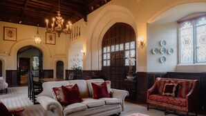 A spacious room with a large sofa, a red armchair, and a tufted ottoman. There are wall-mounted lights and a chandelier.